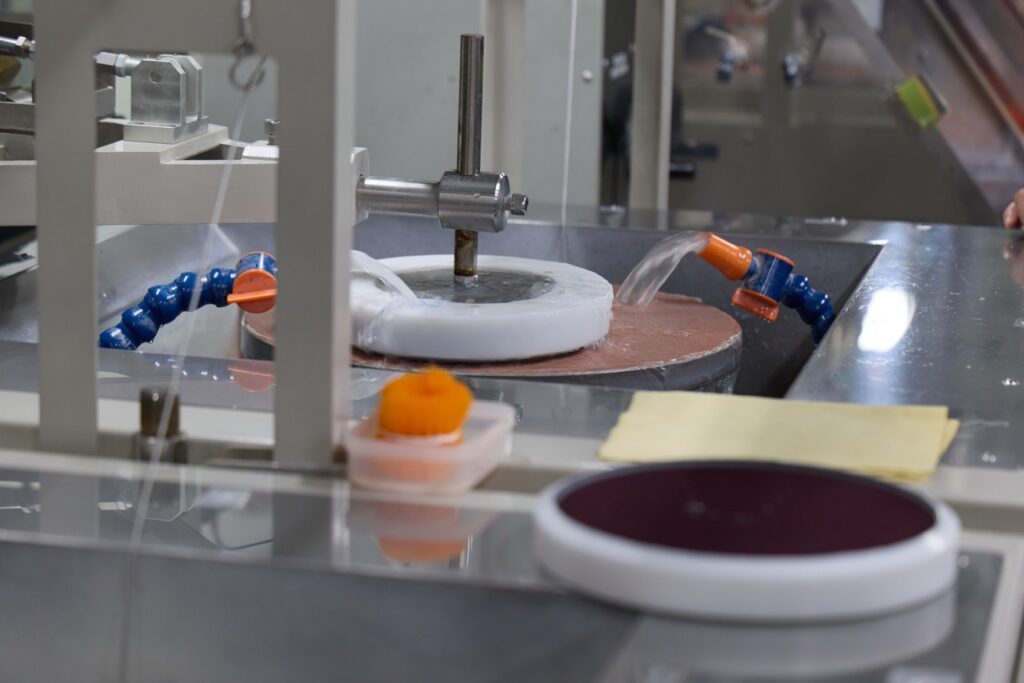 A piece of factory equipment used for making lenses continually sprays liquid onto polishing surfaces.